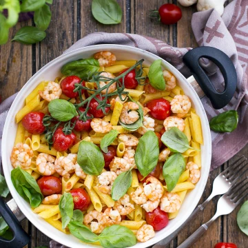 Gluten-free Black Tiger Shrimp Penne topped with cherry tomatoes and fresh basil leaves as a perfect home-cooked meal, which will be featured in a cookbook.