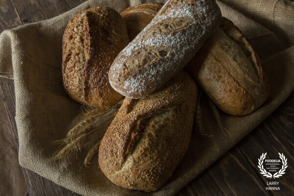 Whenever I am visiting a bakery, I am drawn to the beauty of artisan bread loaves.  Not to mention that I also love to eat it.  The textures and warm colors are amazing.  On a recent visit, I grabbed several loaves and created this image for my own use, using natural window light.