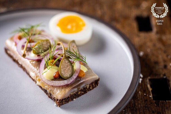 Classic danish open-faced sandwich at the brewery Nørrebro Bryghus in Copenhagen. Here with sea buck herring, together with onion, capers, horse radish foam, smiling eggs, and rye bread. And of course, you should get a schnapps on the side.