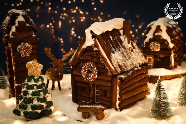 This Christmas, I made a rustic, wintry scene of a village center showing buildings made of cinnamon sticks. The base used is still gingerbread cookie slabs with all walls covered with cinnamon sticks. One house's roof is also covered with cinnamon sticks while the others with black peppercorns and chocolate coins. The Christmas tree and wreaths are gingerbread cookies covered with royal icing and sprinkles;  the powdery snow is none other than desiccated coconut.