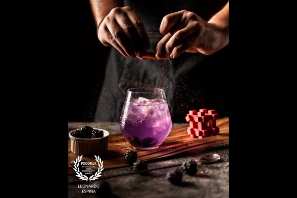 The 'purple' Gin & Tonic masterpiece. Infused with a butterfly pea flower, blackberries and an orange spray. A shot made in a dark lighting set up emphasizing dramatic lights and shadows.