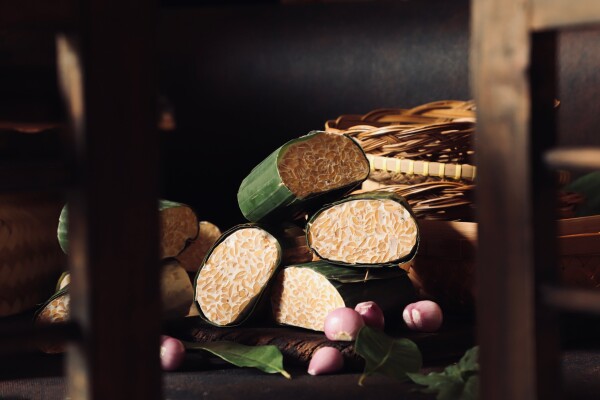 Tempeh or soy bean cake. A very popular vegan protein source in Indonesia. Soy beans cultured and fermented with fungus rhizopus oligosporus which later helps in making the beans into cake form. Traditionally, tempeh is sold wrapped with banana leaf which also imparts its leafy aroma.

Here several chunks of the tempeh are styled with shallots and salam bay leaves, among props of traditional kitchen utensils. A wooden window shutter is placed in front of the tempeh; making an impression of peeking into the kitchen.