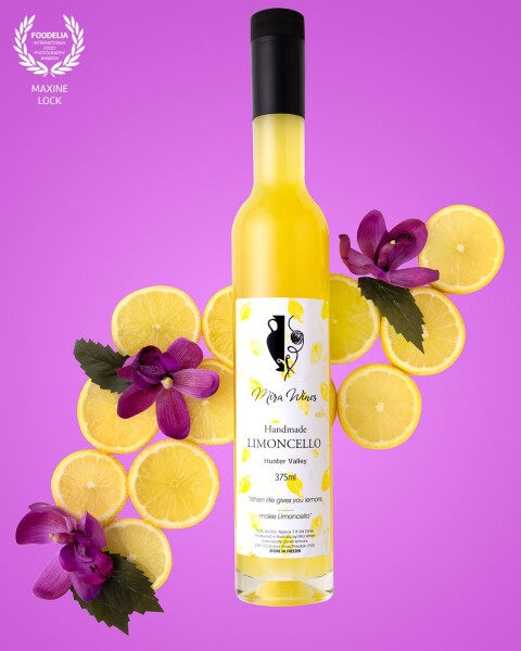 Brightly coloured limoncello bottle photographed with lemons and purple flowers, with a bright purple background for a juxtaposition effect.