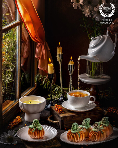 Cozy autumn scene with pumpkin shaped marshmallow, a woman pouring tea, and candles by a window on a rainy day.