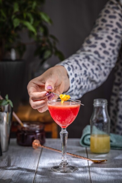 Bartender adding a lemon twist garnish to a vibrant red cocktail in a coupe glass, showcasing the art of cocktail making
