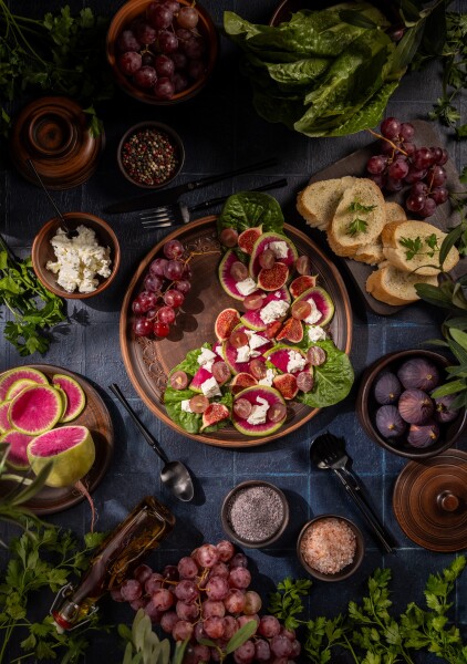 Healthy fresh salad with fruits and feta cheese. Table setting with vibrant salad of watermelon radishes, figs, grapes and feta, surrounded by bread, herbs and seasonings for a rustic, nutritious meal presentation