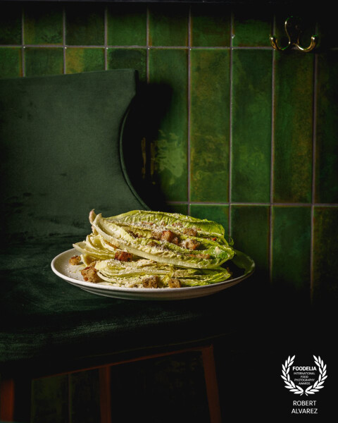 This image stands out for its monochrome green palette, where the tiles, velvet chair, and romaine a...