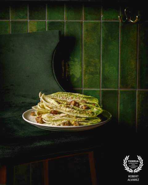 This image stands out for its monochrome green palette, where the tiles, velvet chair, and romaine a...