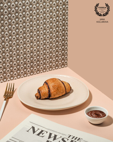 Minimalist breakfast scene with a chocolate croissant on a neutral plate, soft pastel tones, and cle...