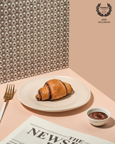Minimalist breakfast scene with a chocolate croissant on a neutral plate, soft pastel tones, and cle...