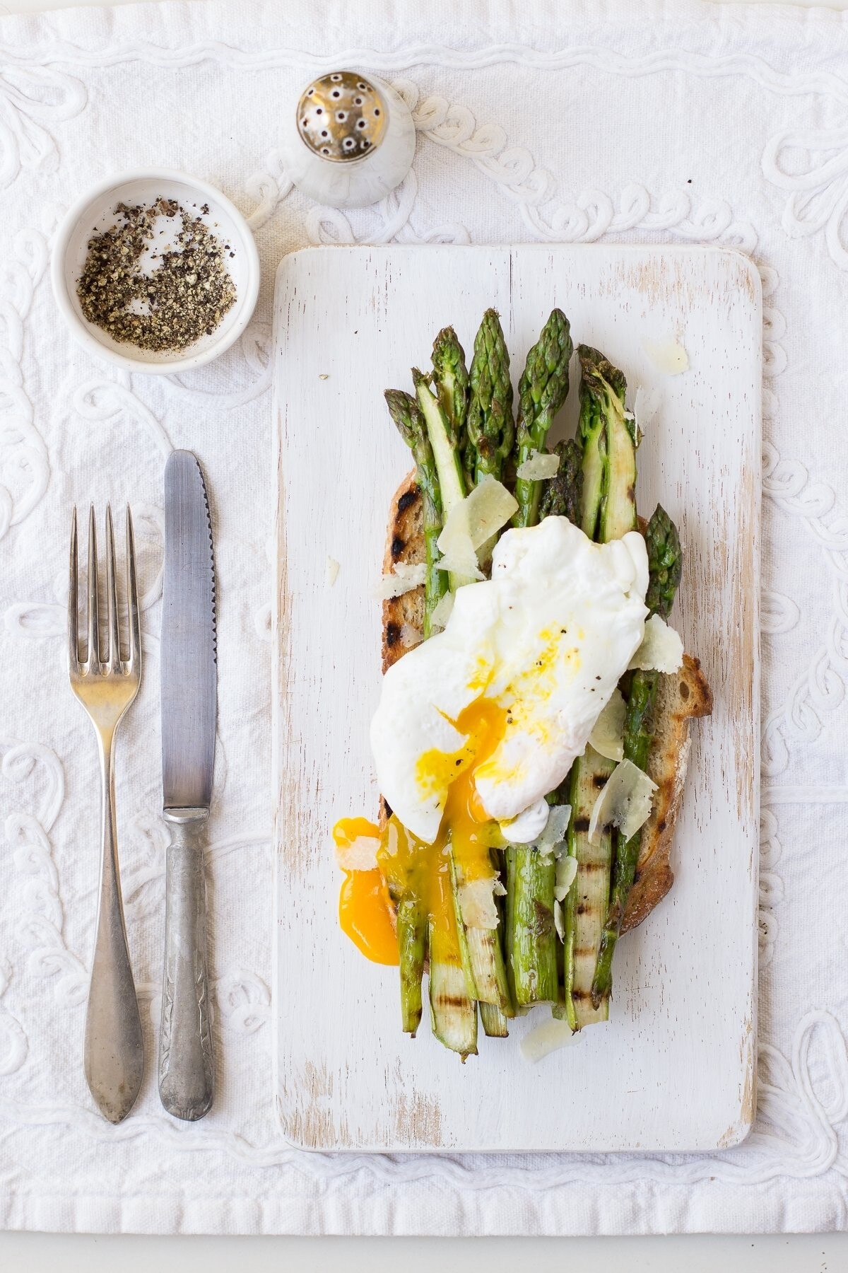 This a photo of poached egg put on grilled asparagus with parmesan and toasted bread. Wonderful spring breakfast. I really love that runny yolk and bright white stylisation.