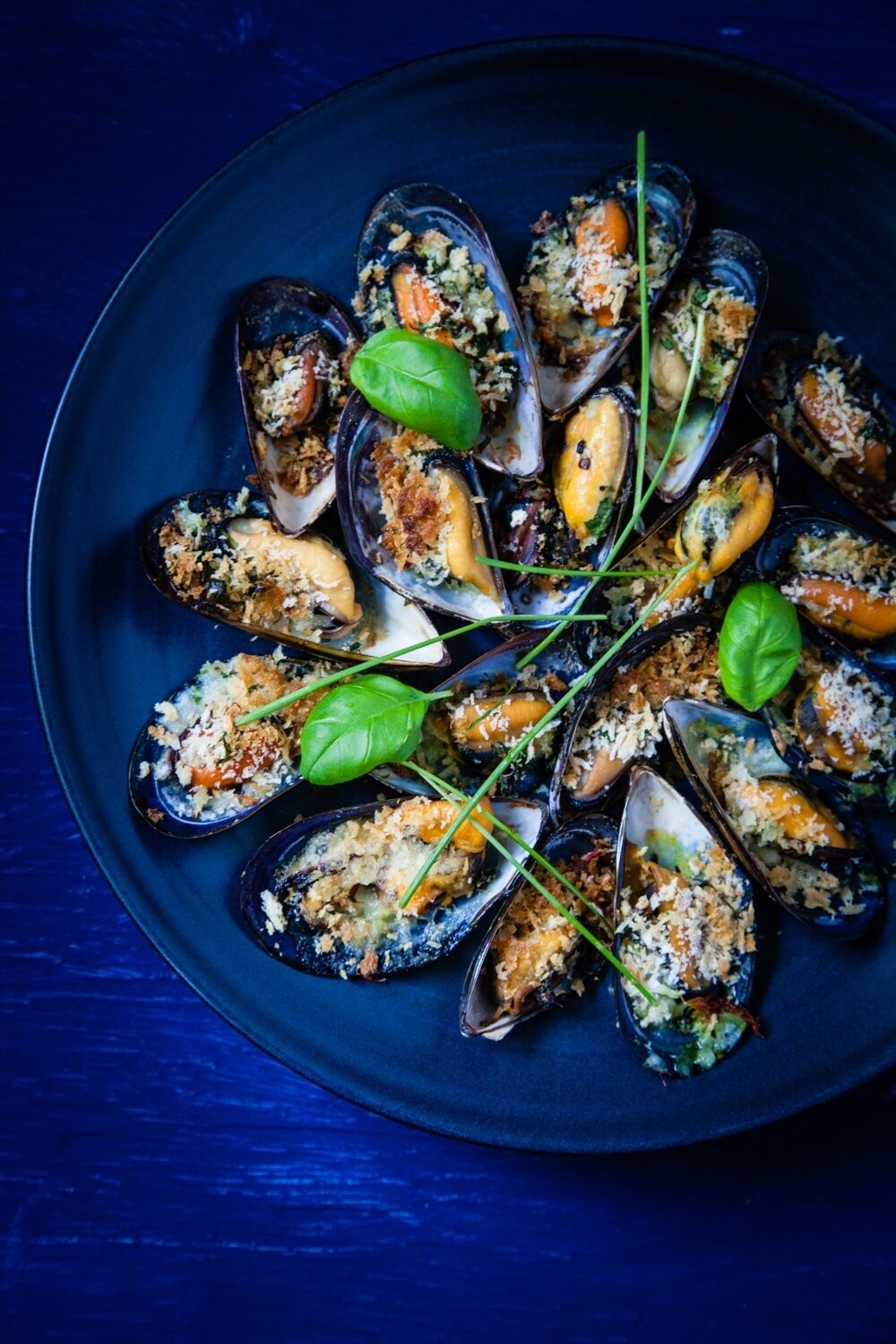 This is one of my favorite shots in my whole portfolio. I love the vivid blue and green colours, and the texture of the mussels in their shells. Mussels Gratinee is a bit of a different dish than the typical shellfish in a white wine broth. They are topped with bread crumbs and herbs and drizzled with a bit of oil before baking in the oven. They’re a perfect, easy starter for a dinner party or an hors d'oeuvre with cocktails.