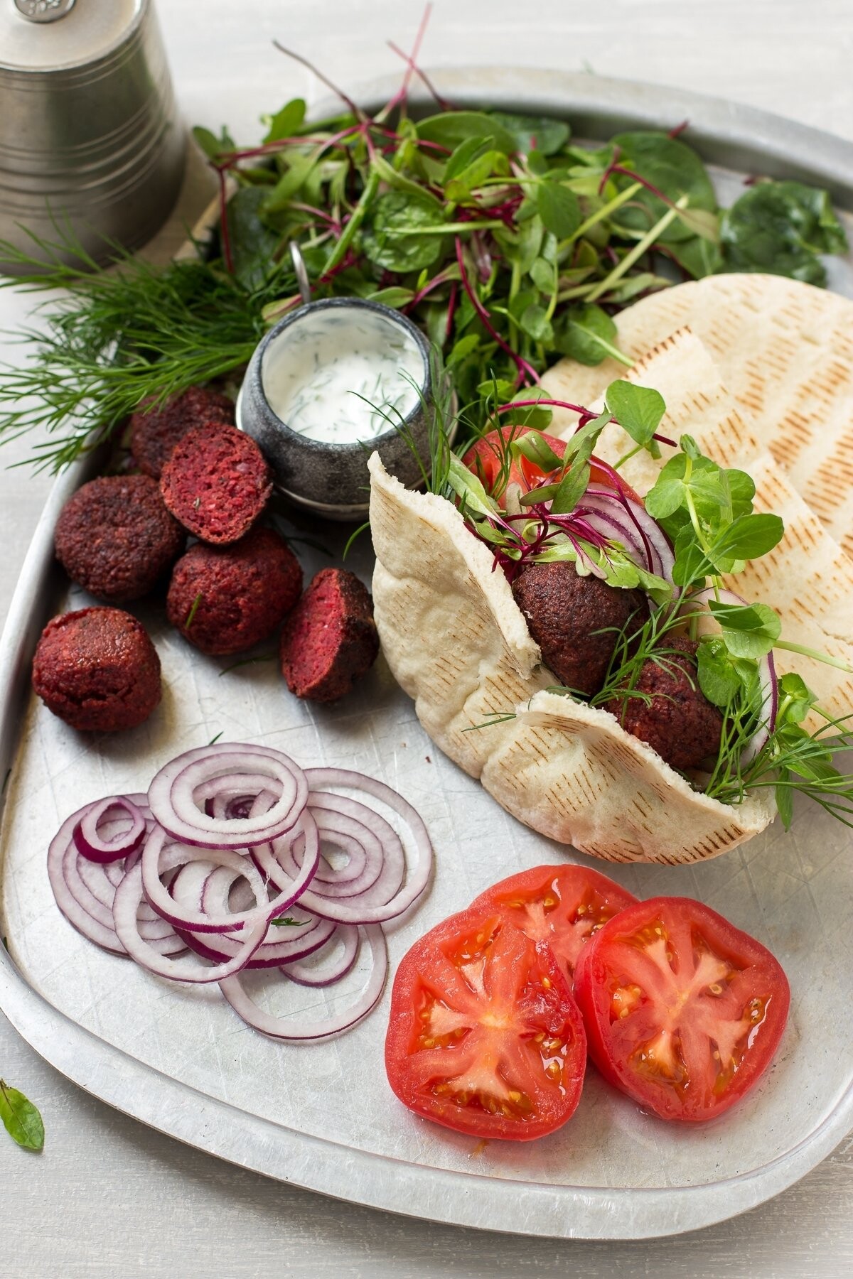 This is a photo of beetroot falafel served with pita, red onion, tomatoes, young beet greens and garlic dill yogurt. I wanted to emphasize the beautiful dark pink color of the falafel as well as the freshness of the veggies, that's why I used neutral background and simple props.