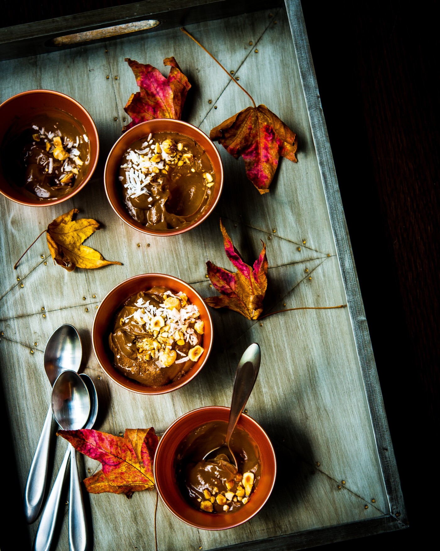 A wickedly scrumptious Mexican chocolate pudding made with healthy ingredients of ripe avocados, unsweetened cocoa, almond milk, vanilla extract, maple syrup and spiced with ground cinnamon, cayenne pepper and Maldon sea salt.  What could be a better way to enjoy this creamy and delectable dessert.  This image is styled with fall leaves and gray tones to accentuate the arrival of the cooler months.