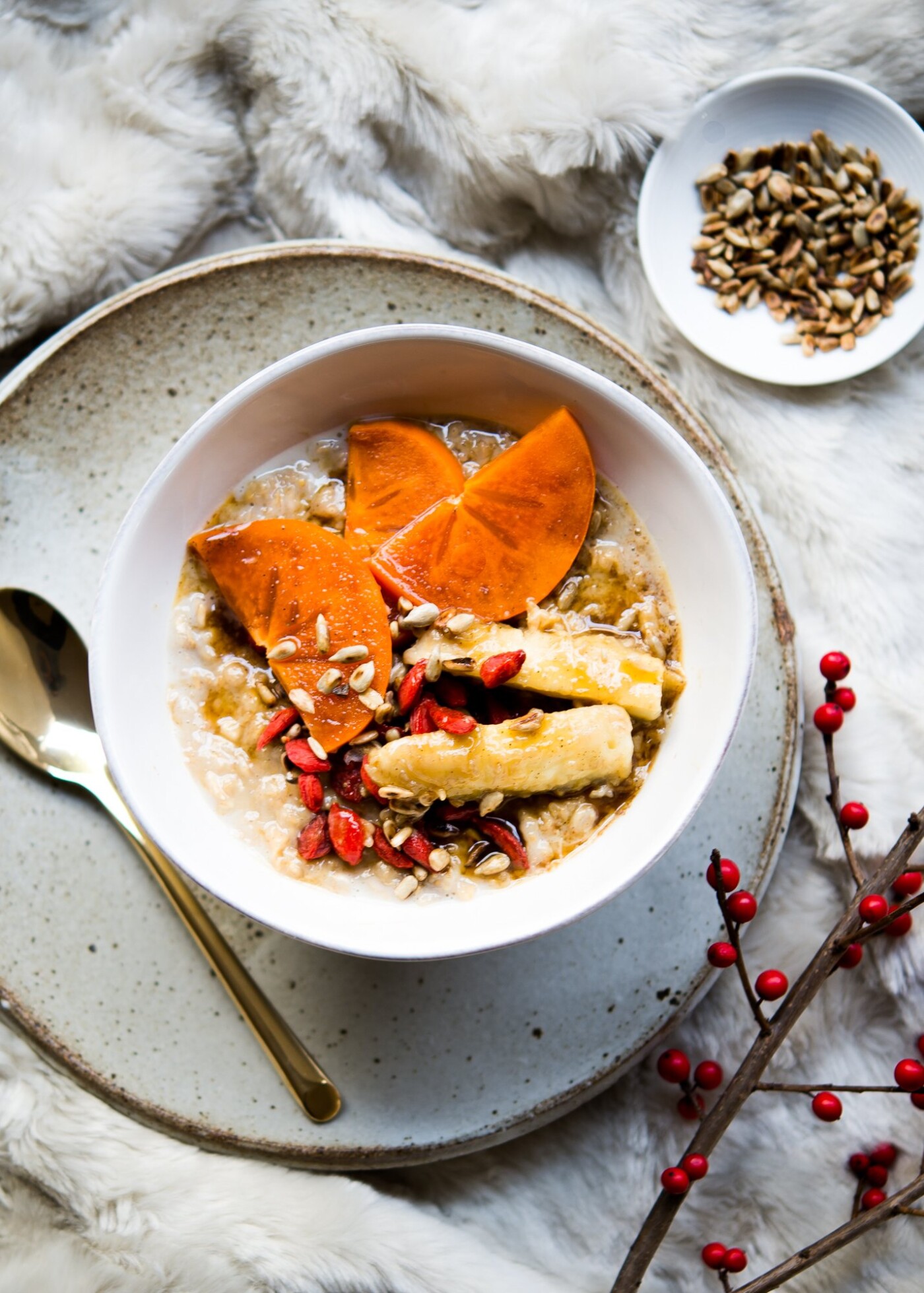 A cozy breakfast for wintery mornings is captured with this warm and hearty chai-spiced porridge adorned with slices of persimmon, chunks of banana, pan toasted sunflower seeds and goji berries.  The fur throw backdrop adds a touch of elegance, texture, and accentuates that warm and fuzzy feeling.