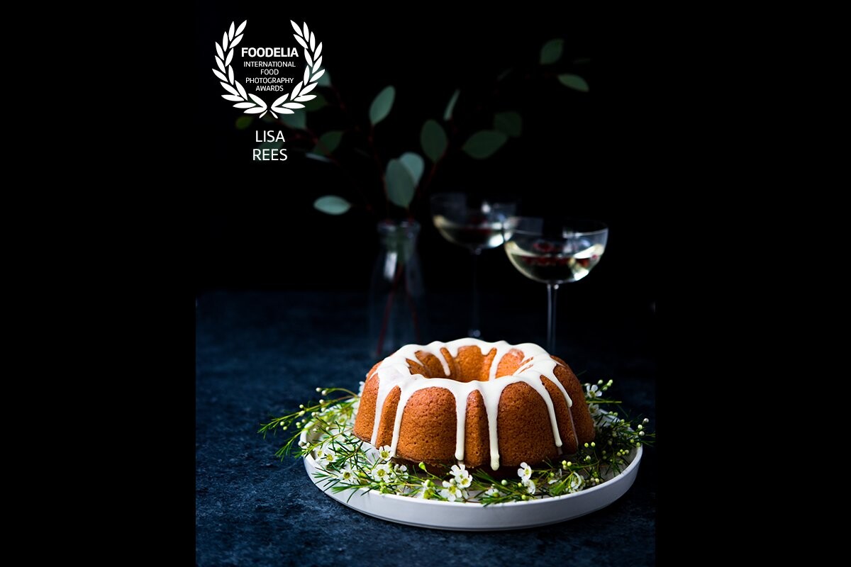 The scrumptious olive oil orange bundt cake takes the center stage in this image.  The twinkling of the eucalyptus leaves in the back ground and the champaign glasses nearby complete the scene with a festive holiday vibe.<br />
  