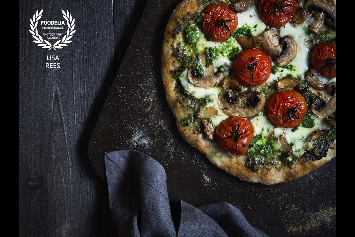 Homemade pizza with a multi-grain dough base, topped with crushed garlic confit, spinach pesto, dotted with torn fresh mozzarella, slices of mushrooms and juicy vine tomatoes.  