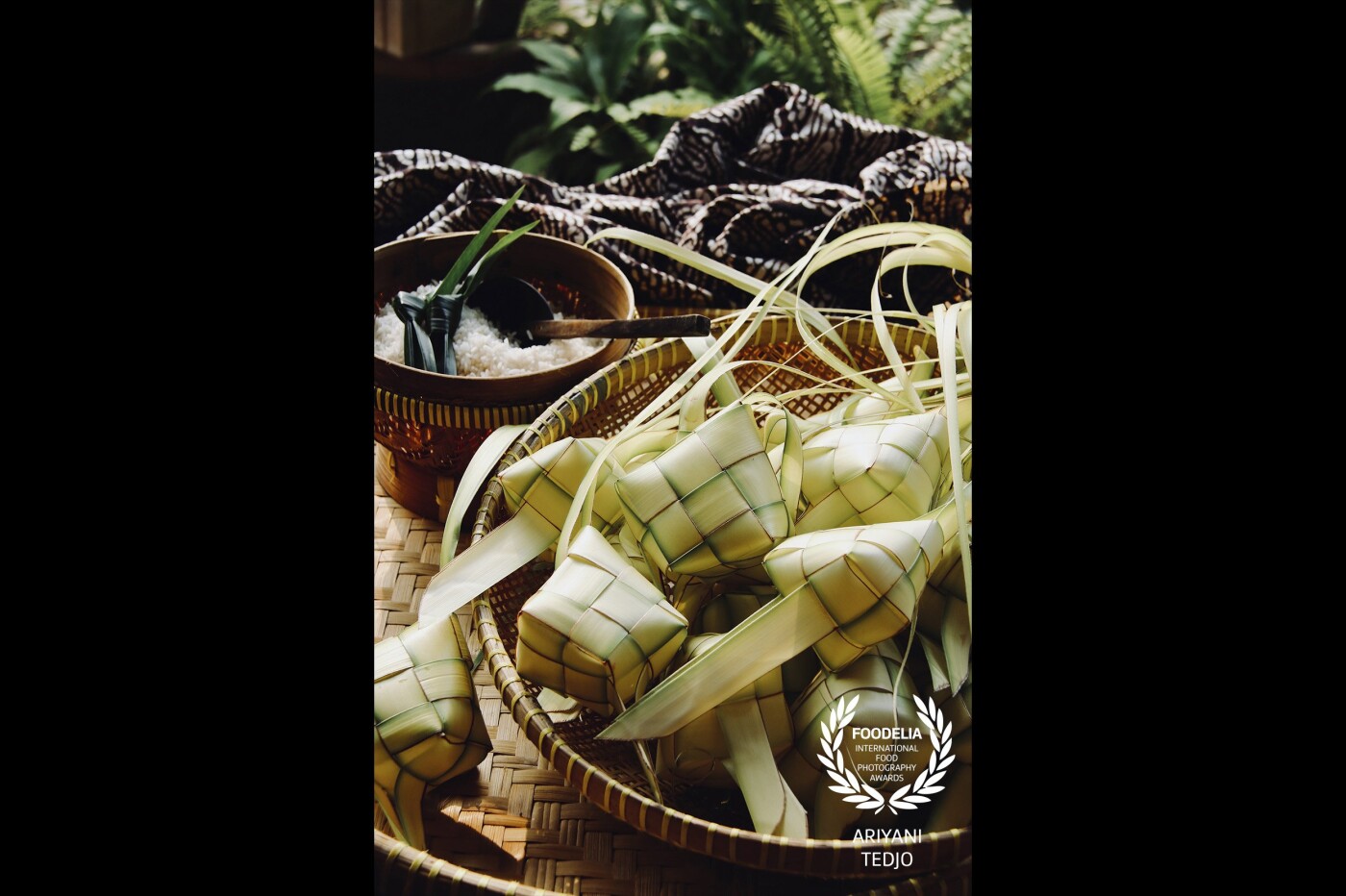 Ketupat, one of several kinds of Indonesian rice cakes which is cooked in diamond-shaped casing made of woven coconut palm leaves. This particular rice cake is popular throughout Java, Bali and also in West Sumatra. Its popularity is increased during the Eid celebrations (with the exception of Bali as majority of Balinese does not celebrate Eid).<br />
Here in the image are dozens of ketupat casings ready to be filled with some rice and then cooked. All the props used in the image are traditional kitchen items used daily at home. The textile in the background is Indonesian Batik cloth.
