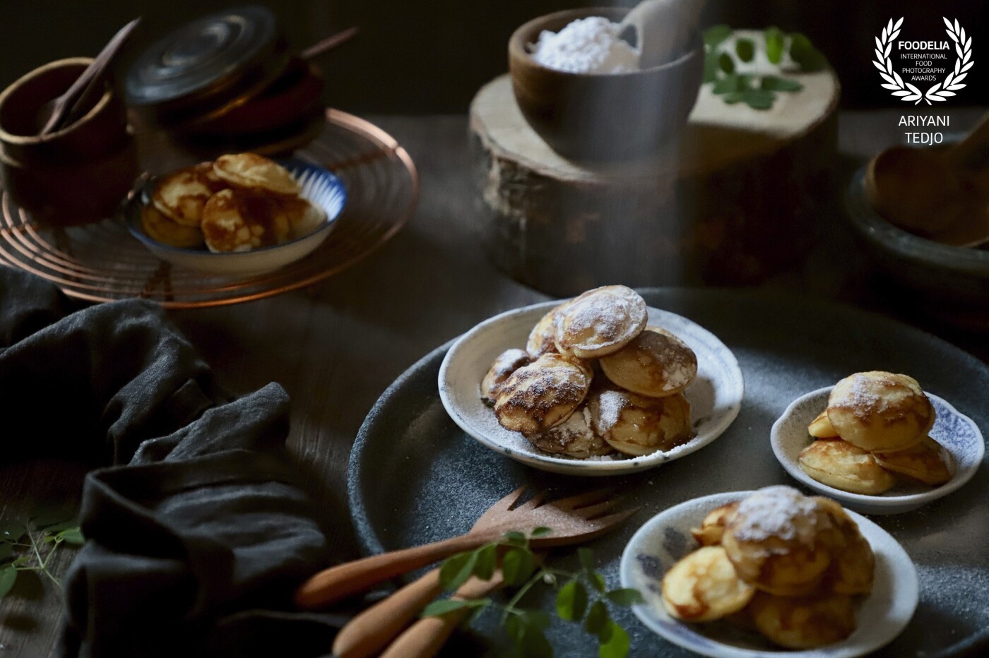 Sugaring the Poffertjes.  This little snack is a favorite in the family. Originated and popular in the Netherlands, it is also popular in Indonesia as a former Dutch colony. <br />
<br />
The poffertjes are plated in several small plates in various sizes and styled in a moody dark scene. 