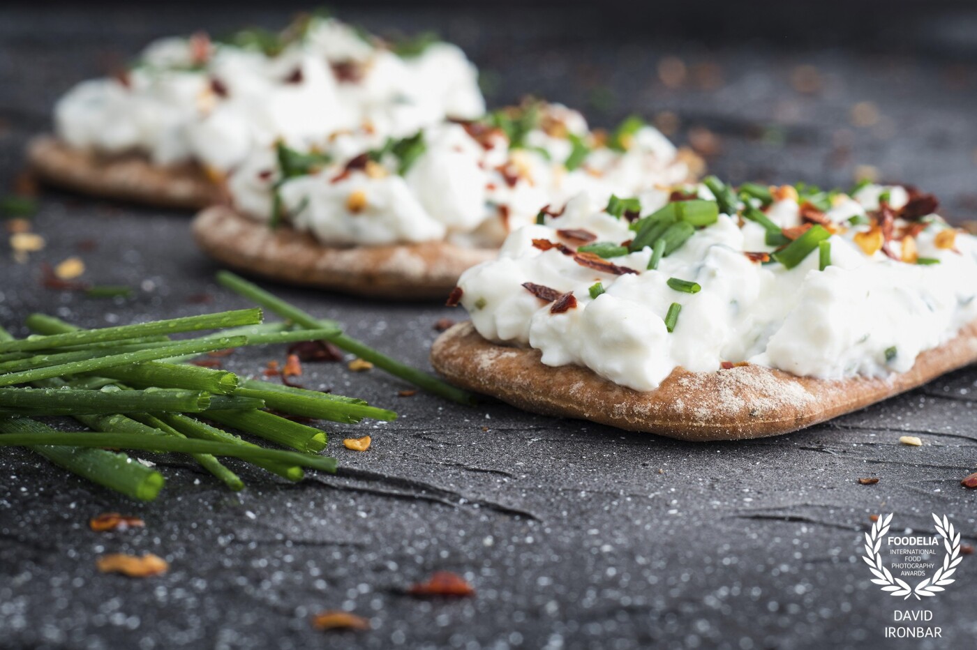 Cottage Cheese with a sprinkle of Chilli flakes & Chives on rustic biscuits, taken in natural light.                                <br />
