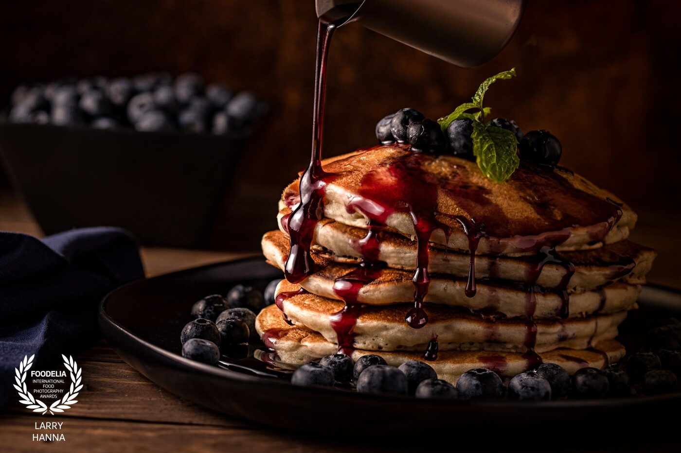 I love a stack of blueberry pancakes in the morning and recently bought some blueberry syrup and loved the way it enhanced the beauty of the pancakes. I decided that I needed to create an image emphasizing the syrup. I created this image in my home utilizing strobe light to freeze the action of the pouring syrup