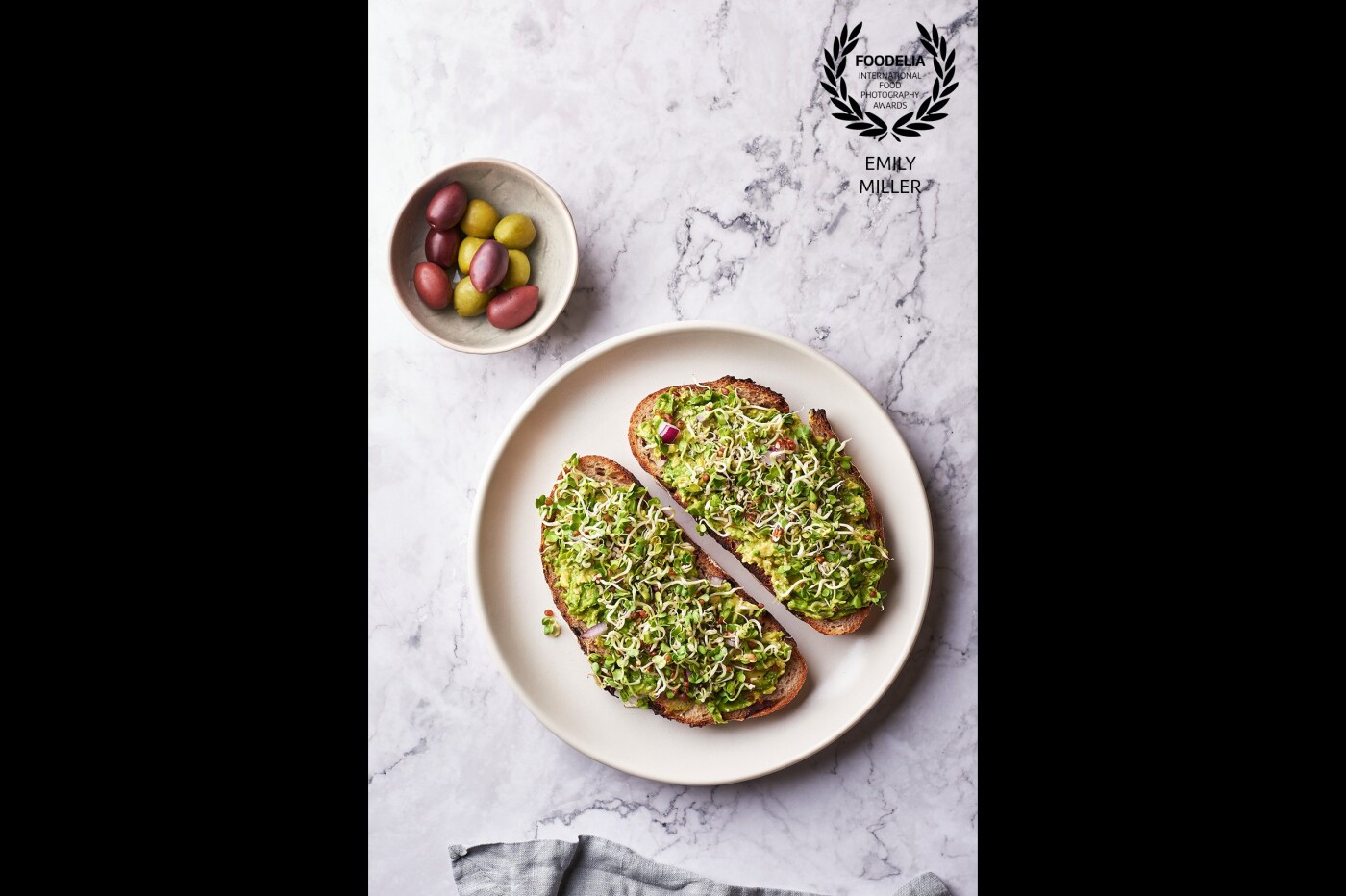 This photo is avocado toast made from homemade olive sourdough bread topped with chopped red onion, sea salt, and homegrown radish sprouts. This top-down shot was taken with artificial light (strobe) at around the 11:00 position.