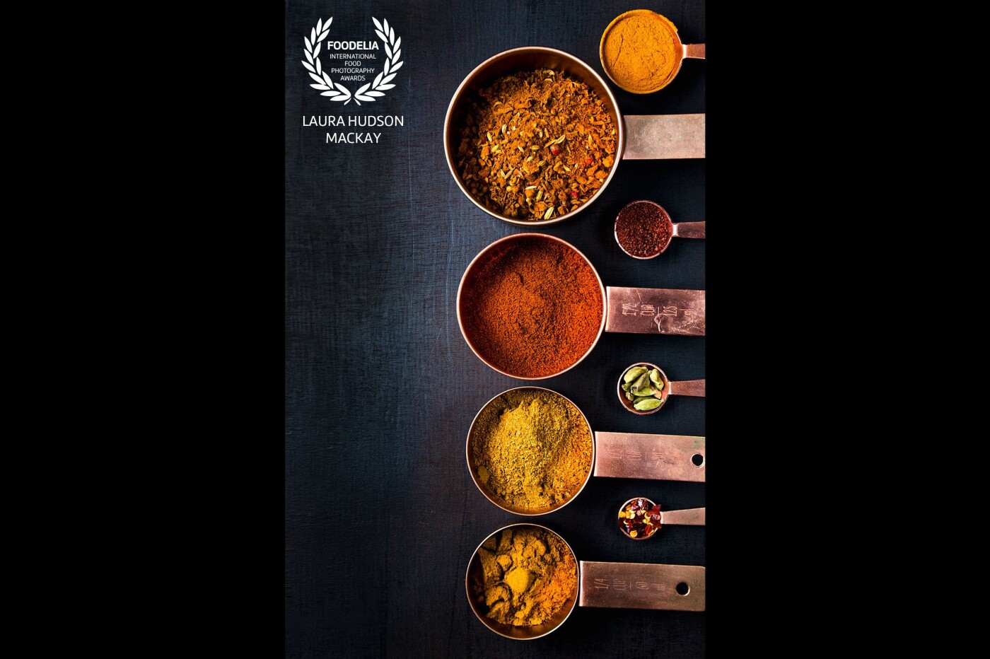 A collection of bright spices on a dark background, sitting in well used copper measuring cups. My favourite spice is Ras-el-Hanout, this Arabic name translates as 'The best spices in the shop' or 'Top shelf'.  A Moroccan spice blend created using the best the dealer has to offer. <br />
