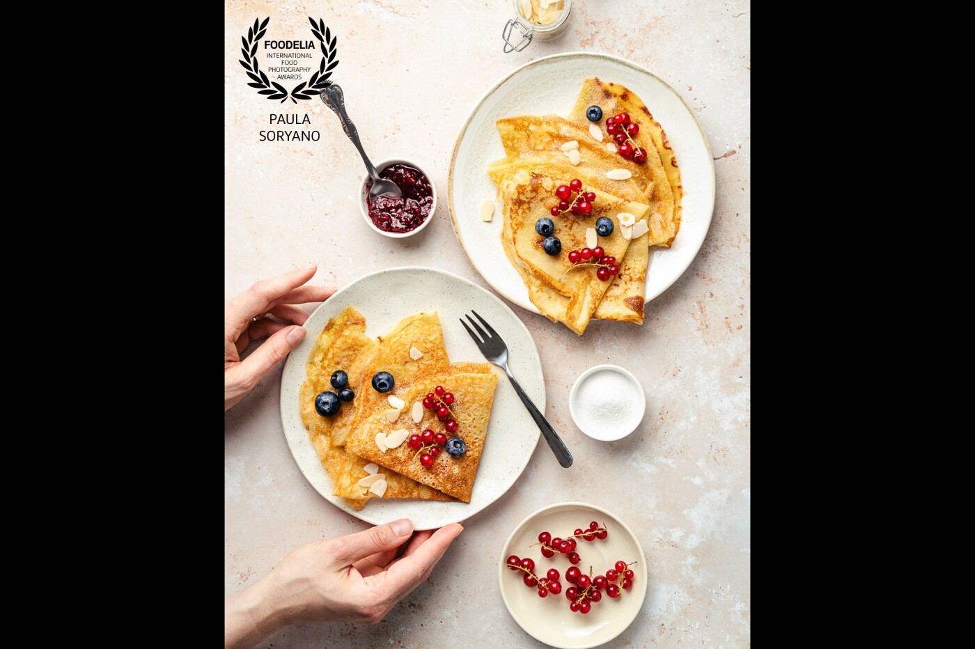 Join me for this summer crêpes party. <br />
A flatlay with homemade crêpes, styled with berries, sugar and almonds. <br />
I wanted to achieve something soft, airy and colorful, without ignoring the beautiful light-brown of those delicate layers. Sugar or jam for you?