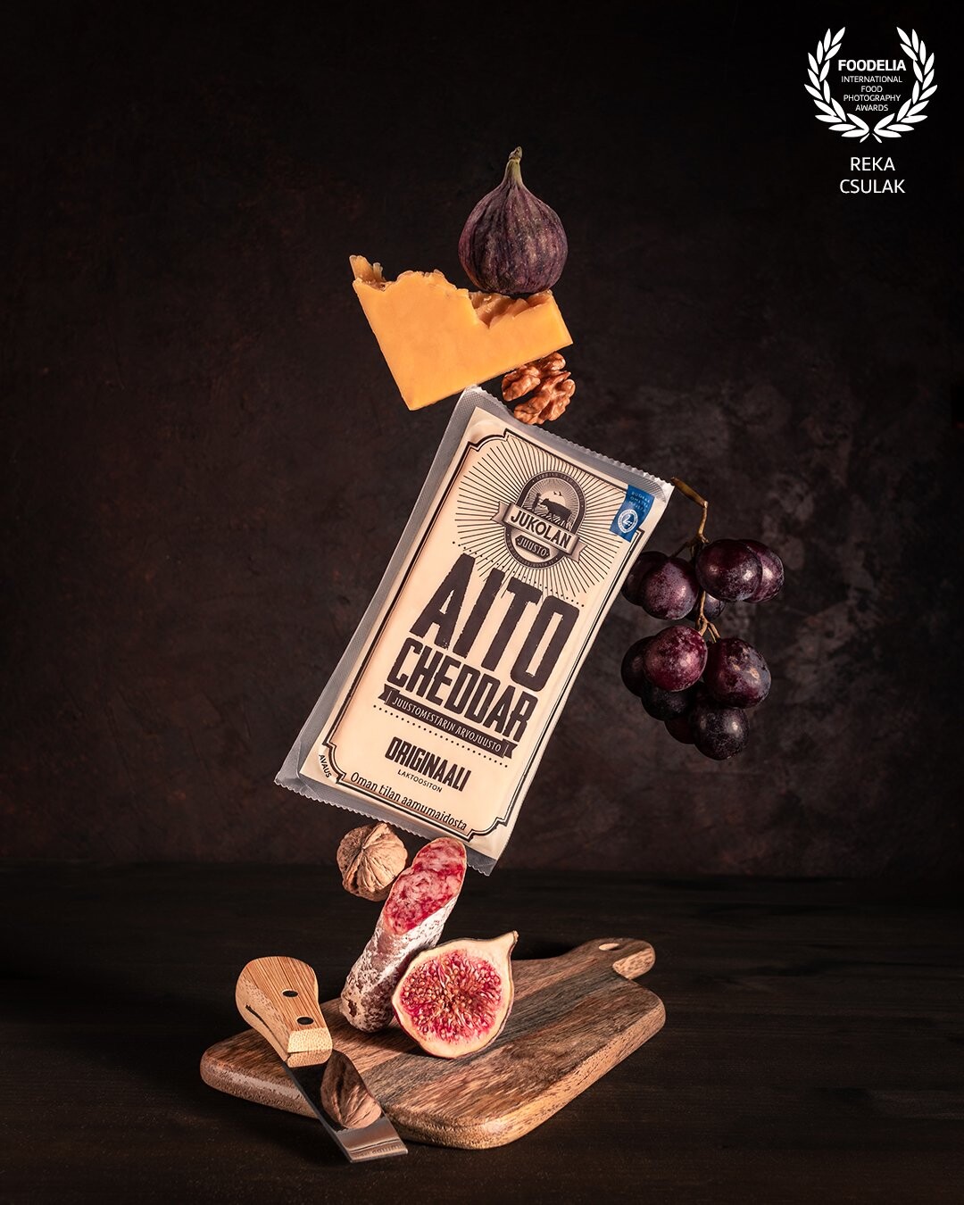 Cheddar and cheeseboard ingredients - grapes, salami, figs, nuts- are in balance, while the product is in the center of attention.