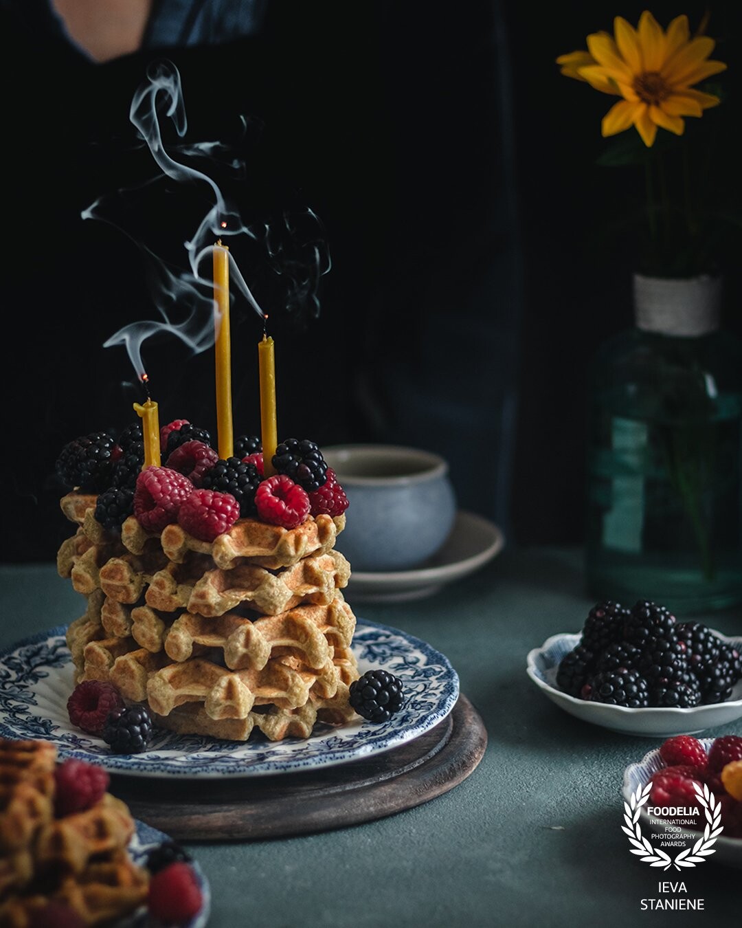 I wanted to create moody and a little bit festive atmosphere in this image. The neighboring colors of the backdrop and props, the dark background, layering and some smoke helps to catch the attention on the waffles.