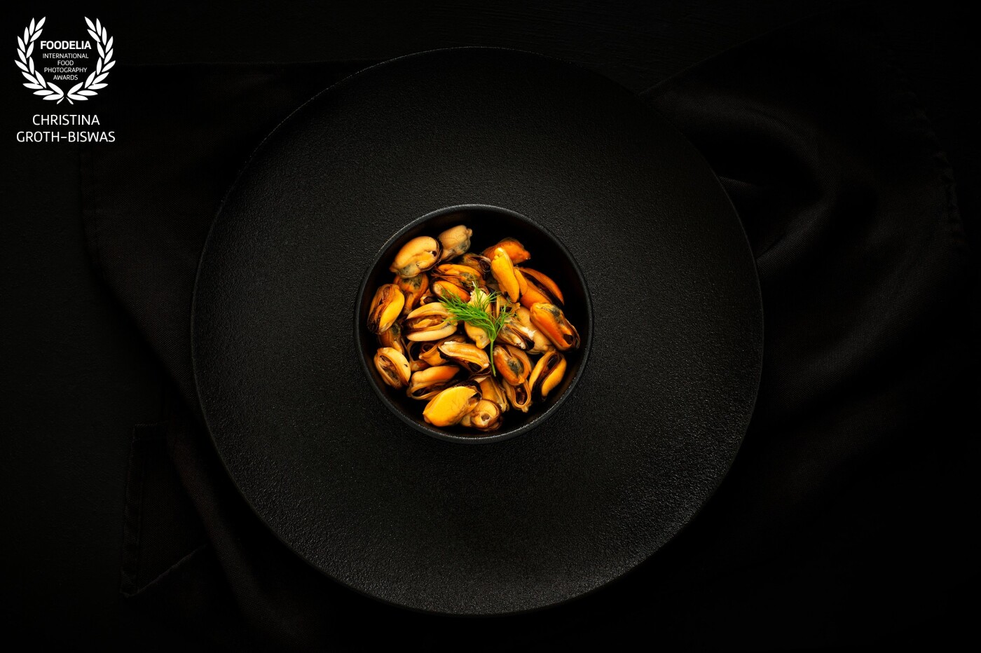 A bowl of cooked mussels on a simple black set up, which I believe enhances the beautiful almost golden colour of the mussels without adding additional distractions.