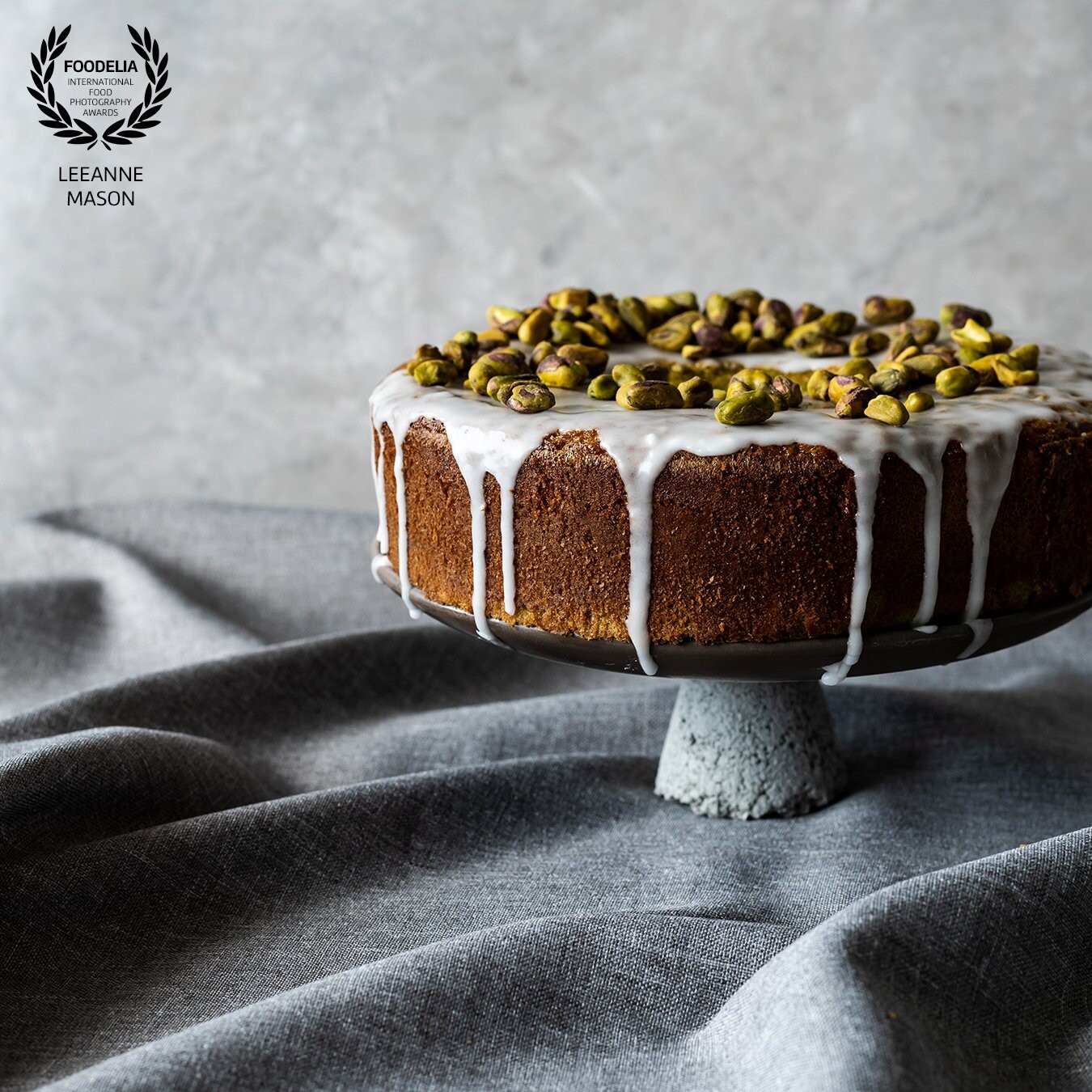 This is a delicious Pandan Cake made in a Chiffon Tin with a simple drip glaze and pistachio topping.  The use of negative space helps draw the viewer to the visual weight of the cake.  The detail of the cake and the fabric base is highlighted by lovely soft natural side light.