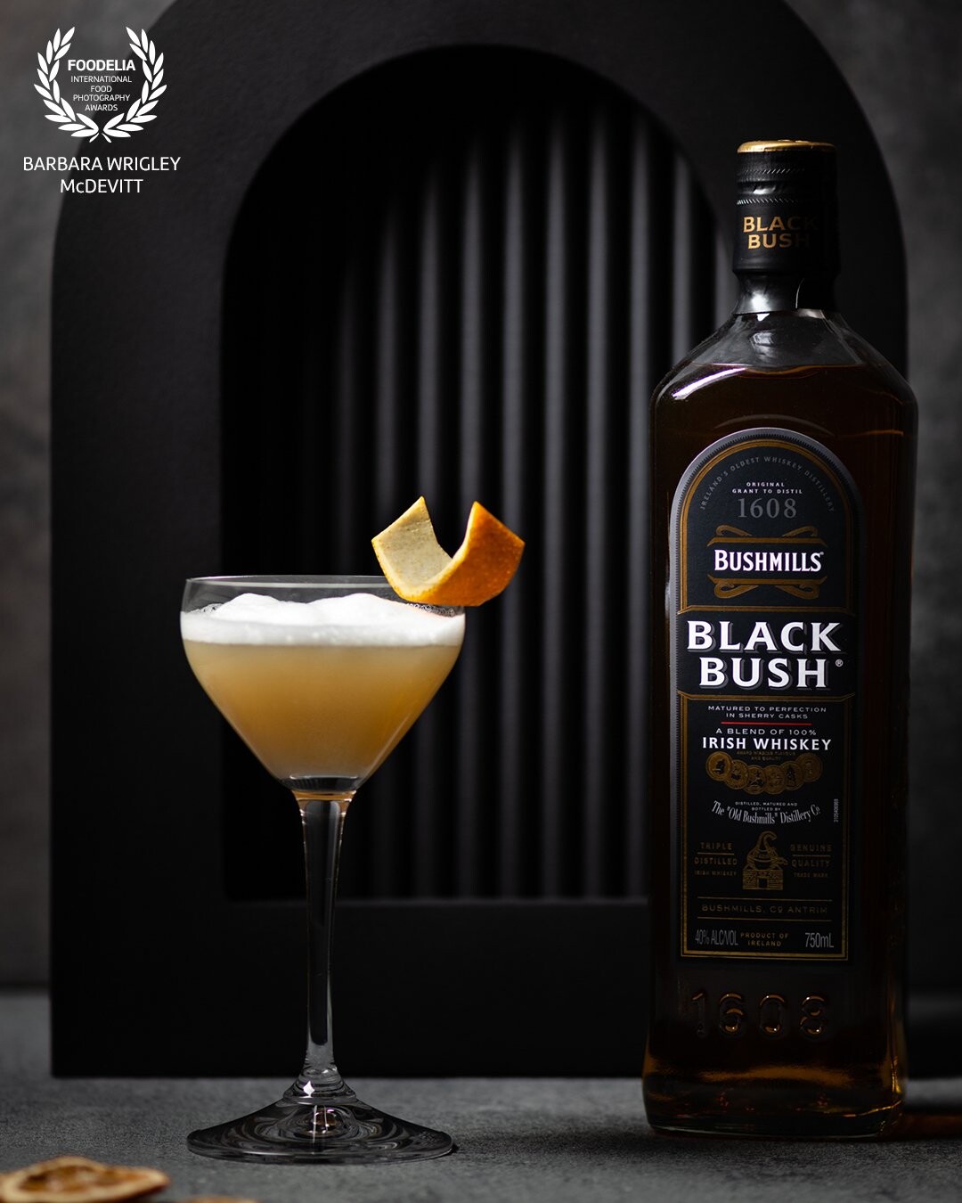 I wanted to display this cocktail and the Bushmills in a unique way.  I selected a grey textured background and used black geometric shapes to give the image dimension without distracting from the cocktail.  I also focused the light on the upper portion of the drink and the Bushmills label to draw the focus to the cocktail and to recess the geometric shapes into the background.