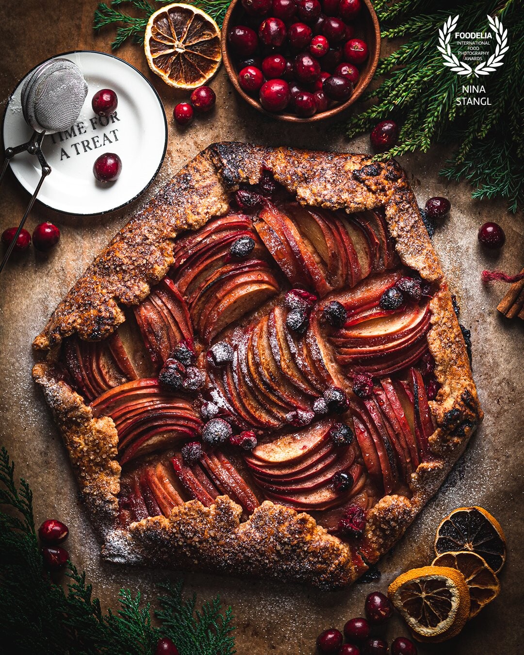 I love creating flatlays. This flatlay was created during the Christmas season . It’s my sisters apple. Cranberry galette with a whiskey frangipane. I added the evergreens to create a holiday seasonal image .