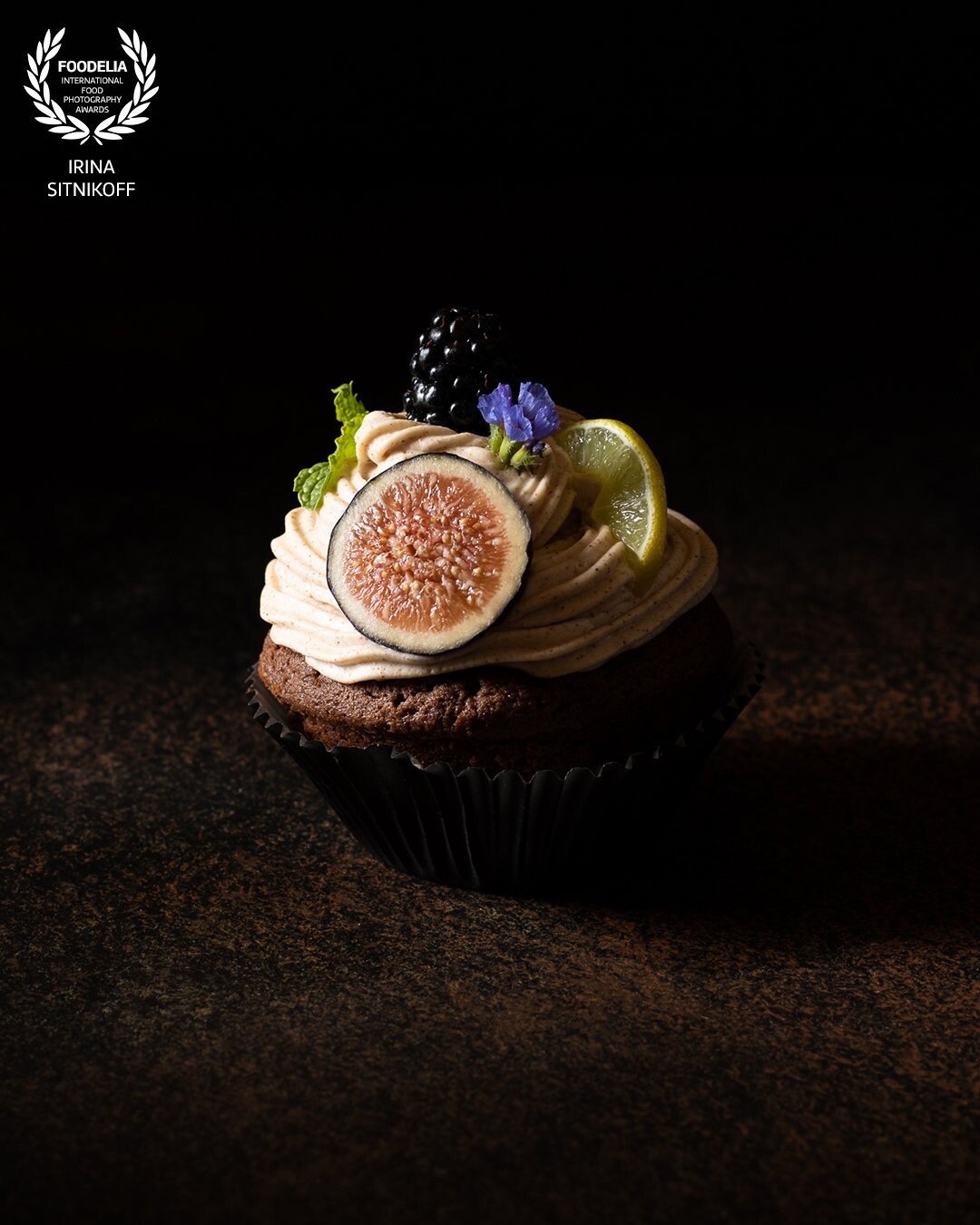 I have always been mesmerized by dark food photography which creates magic and mysterious atmosphere. I have developed and photographed this recipe of Chocolate Cupcakes with Hazelnuts & Cinnamon Cream Cheese for my Instagram culinary blog and decided to shoot it in minimalistic style to show off the beautiful presentation of the product itself, without any distractions on the background. This photo was shot in August and represents the last breath of summer, a sweet season of figs & berries.  The soft chocolate sponge cupcake covered with silky and smooth cinnamon cream cheese with vanilla, accompanied by adorable aromas of figs, berries, mint & lime - the taste is irresistible. I wanted to express that feeling in this photo.