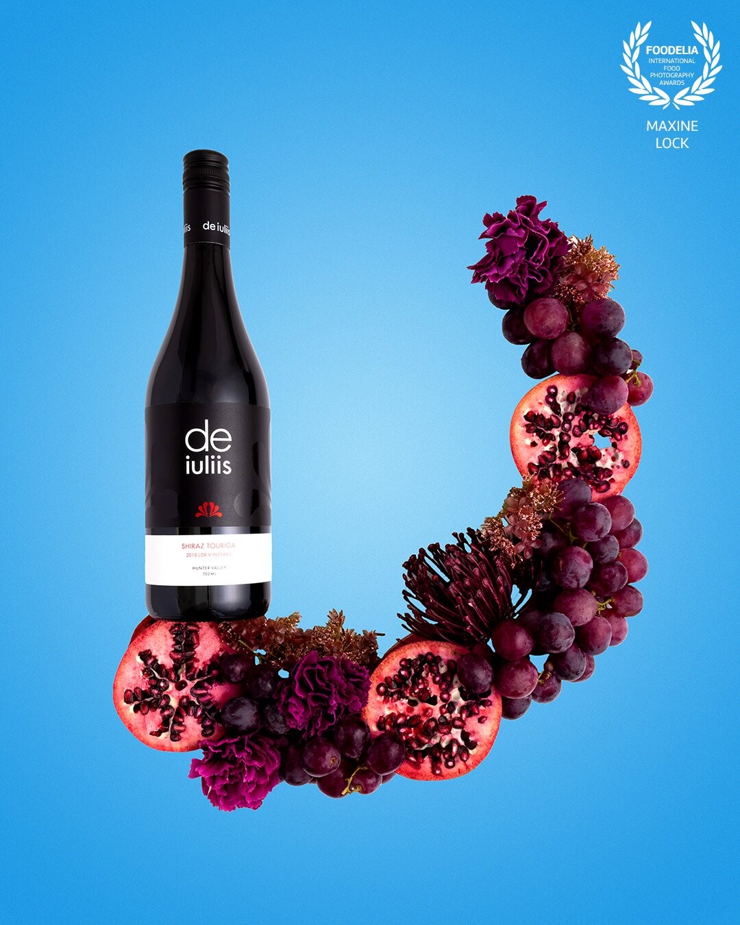 Using red grapes, along with red flowers and other red-coloured fruits, to symbolise the rich redness of the bottle of red wine.