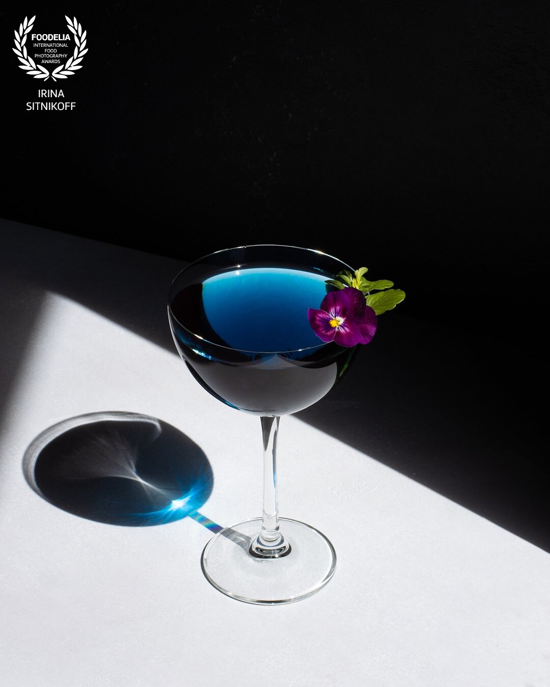I love working with hard light and so glad I managed to catch a sunny day to take this photo. Inside the glass is Butterfly Pea Flower drink, the deep blue drink color created an amazing shadow. I decorated the glass with a delicate fresh pansy which complements the blue color so well. The beauty is in simplicity.