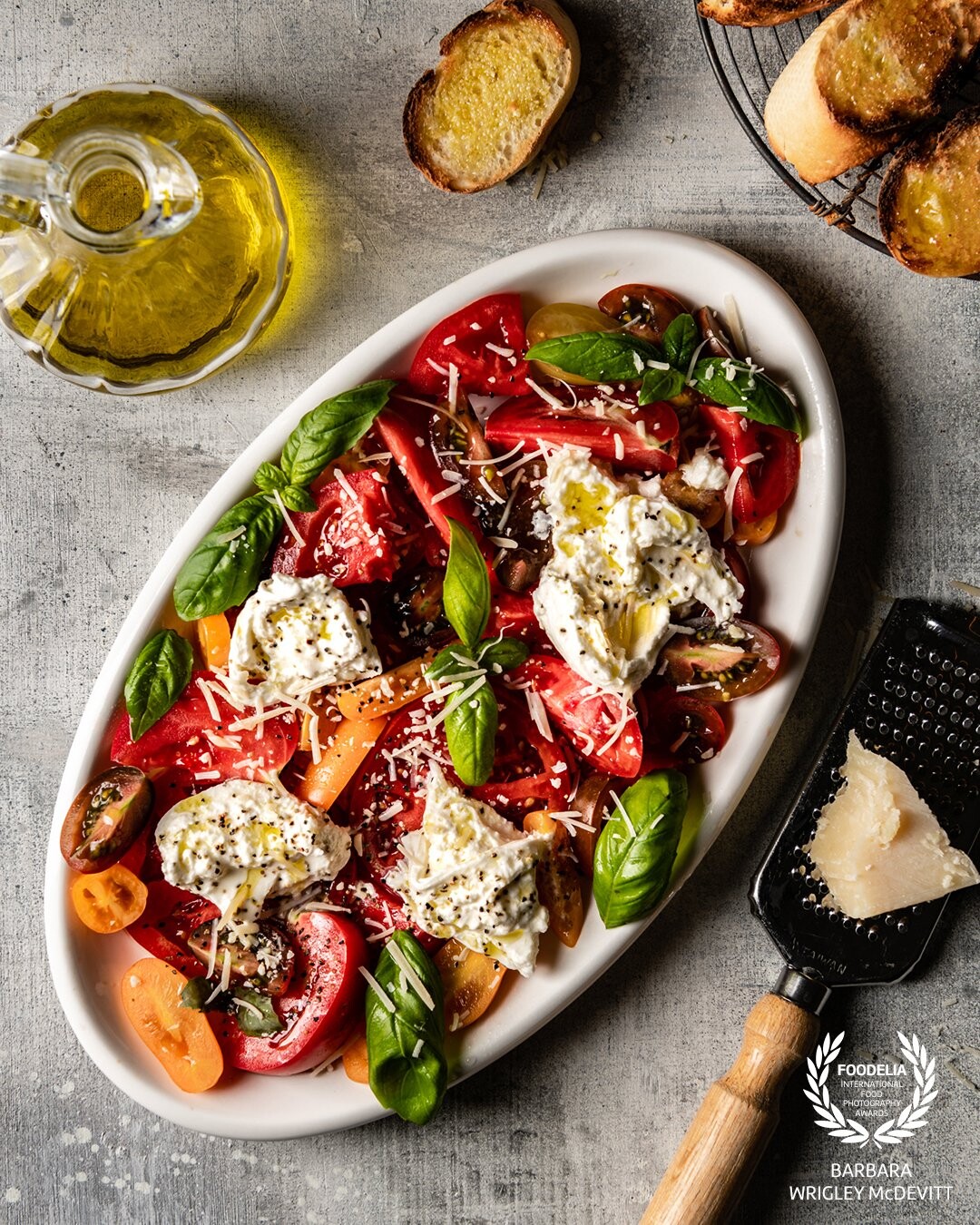 Nothing better than a ripe tomato salad with plenty of fresh basil, burrata and Parmigiano-Reggiano cheese.  Crusty bread to sop up the olive oil goodness completes this healthy dish.<br />
<br />
Shot with Nikon D850 on a 24-70mm lens and Profoto B10 artificial light with rectangular softbox.  Light positioned at the 11:00 position - my favorite.