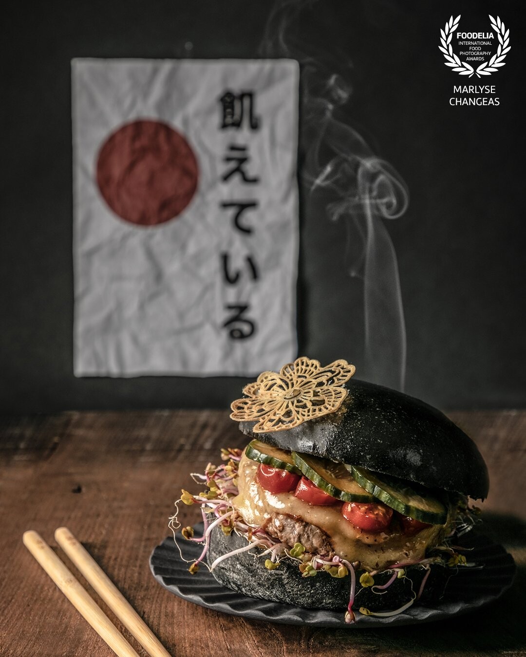 Cette photo à été réalisée pour un concours culinaire. Le thème du concours est la street food et le cuisinier a décidé De mettre en avant la cuisine japonaise.<br />
Je souhaitais mettre en avant la texture du burger par la lumière, un petit clin d’œil à l’arrière avec l’écriture en japonais du nom de son entreprise. <br />
Le mouvement de la fumée nous donne l’impression que le burger est prêt à être dégusté.