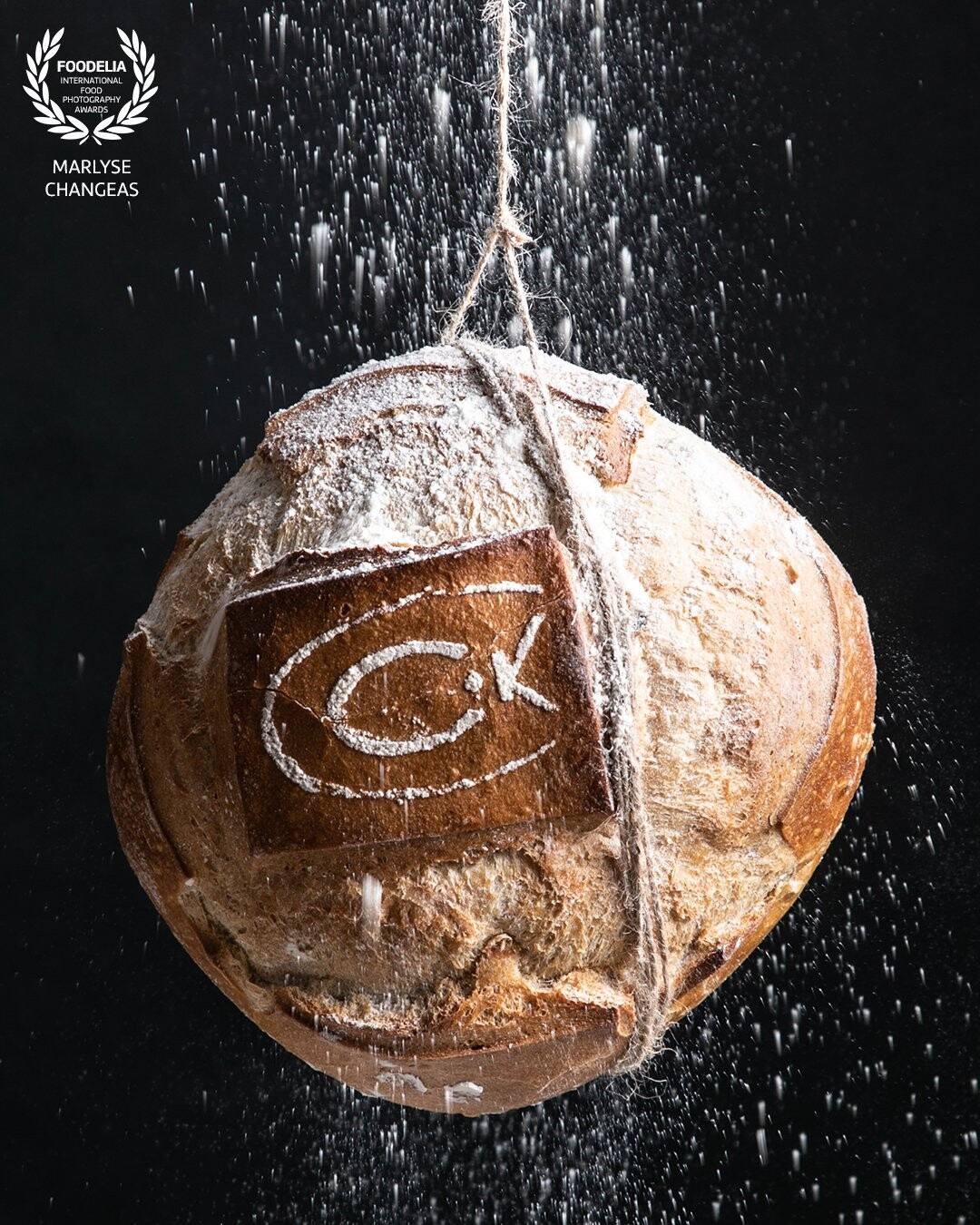 L’idée était de suspendre un pain au milieu d’un jet de farine pour apporter de la modernité à cette image. Une source de lumière latérale et un fond noir sont utilisés pour rendre le pain le sujet principal