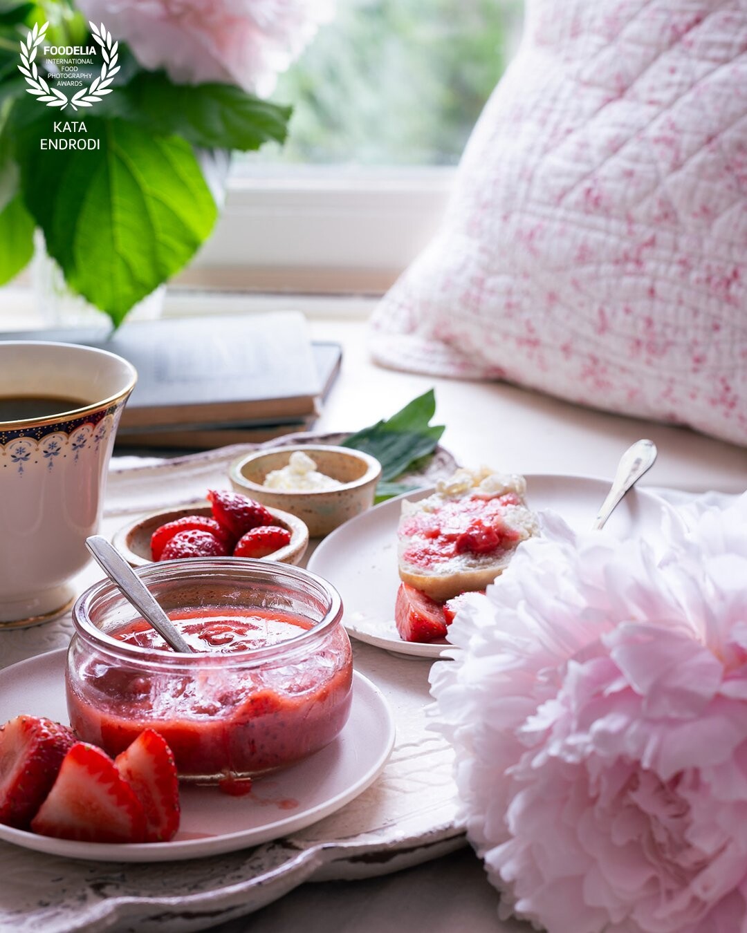 Cozy pink breakfast still-life: strawberry rhubarb jam, toast and coffee, with the suggestion of a view into a summer garden. Fresh peonies complete the scene.