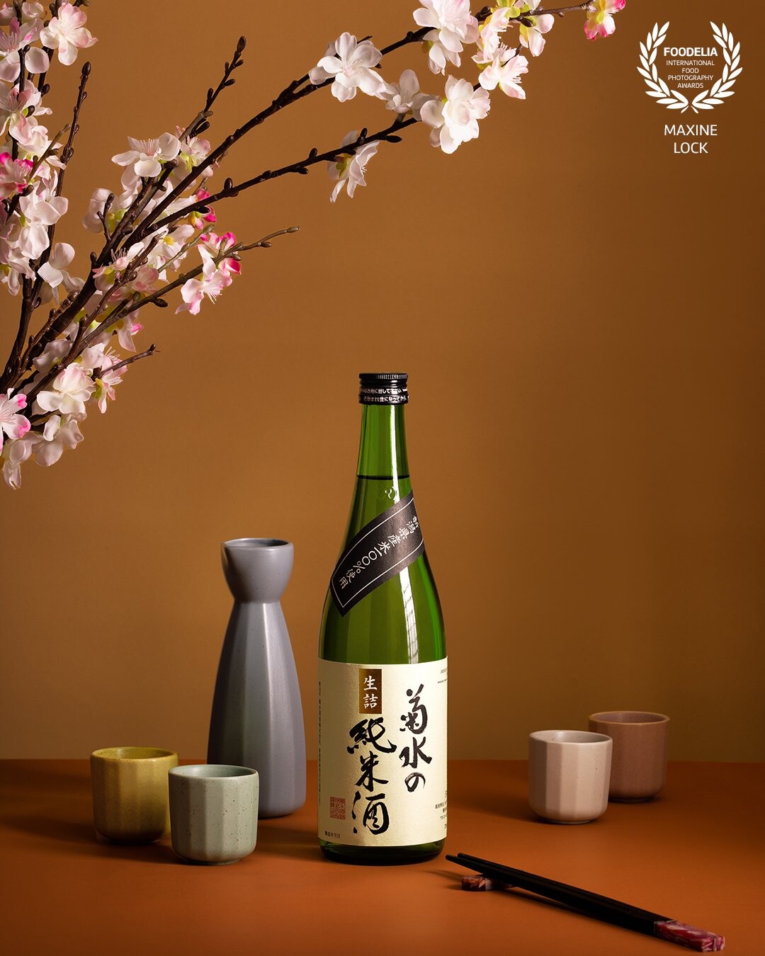 A beautiful bottle of sake with a set of sake vessel and cups used as props in the image. Sakura flowers added into the scene for some depth and interest.