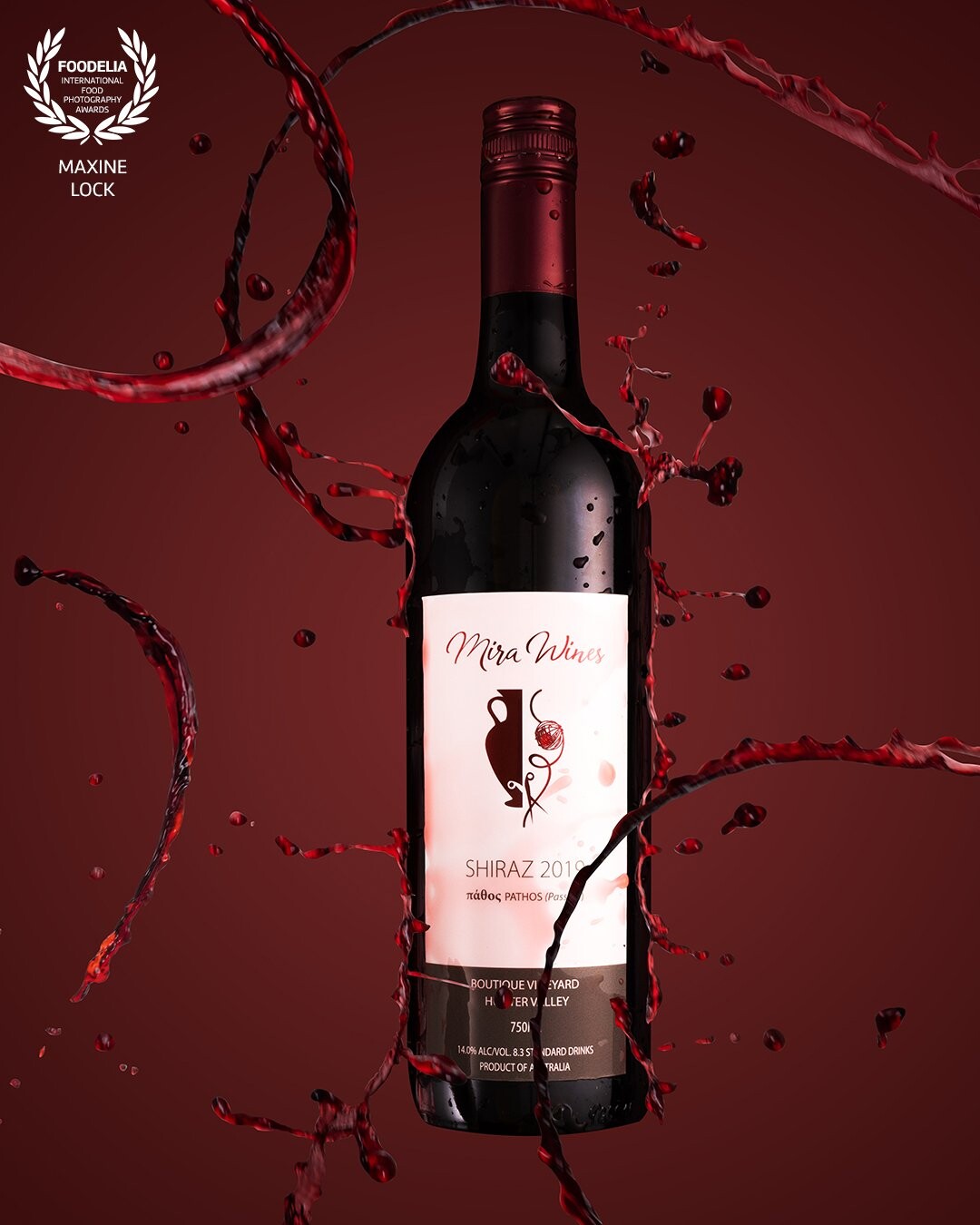 Bottle of red wine, with red wine splashes creating an illusion that the splashes are both hitting against the bottle, as well as being splashes around the bottle itself. All against a red wine colour in the background.
