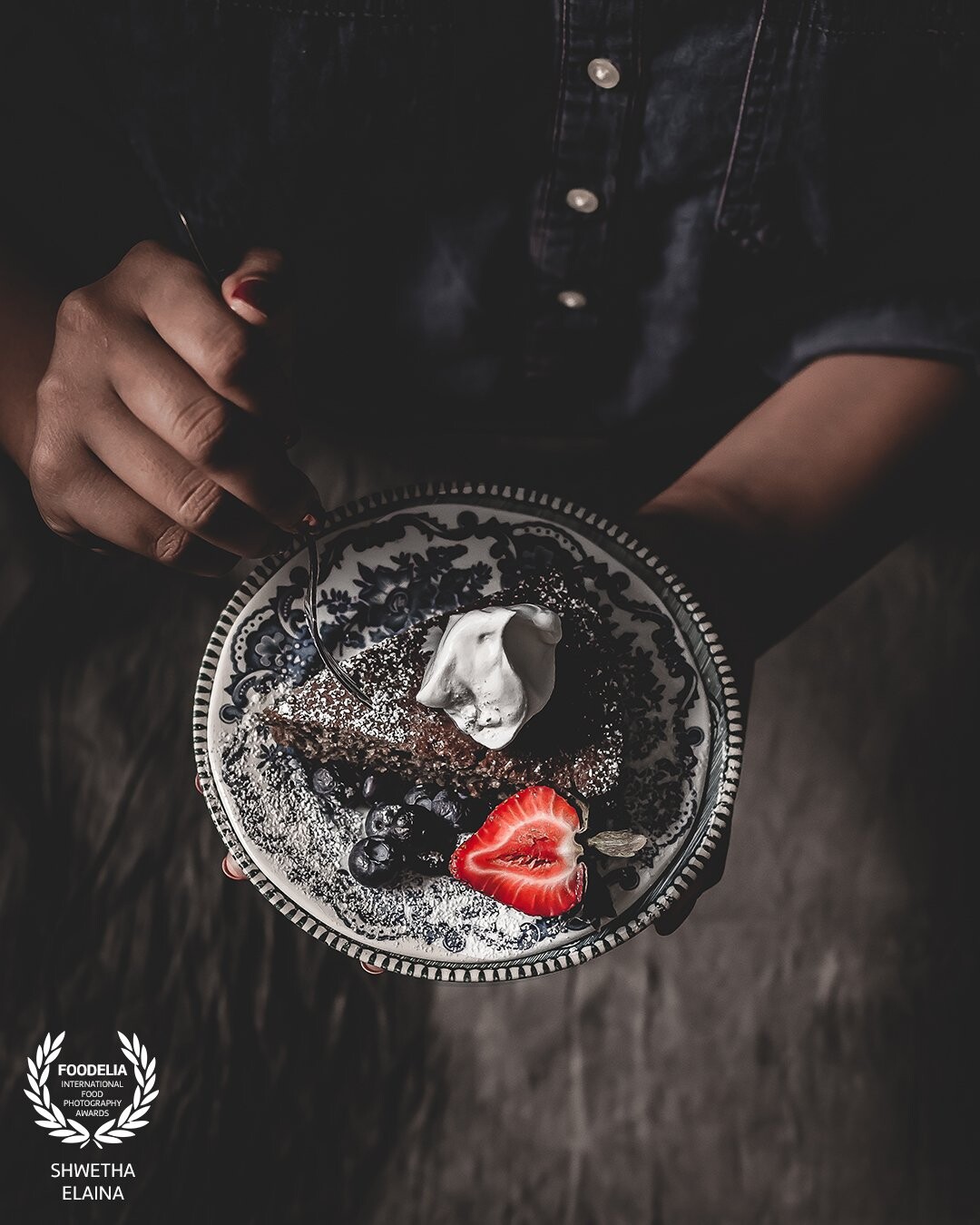 A slice of chocolate sponge dusted with powdered sugar, topped with fresh cream and strawberry. An attempt to capture an inspiration for a monthly food photography challenge.  An exploration of a ‘different from the norm for me’ approach to food photography.