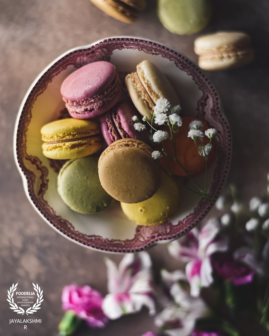 Colorful Macarons set amidst flowers . Shot  in natural light in a moody set up . Created some depth in  the frame by adding layers.