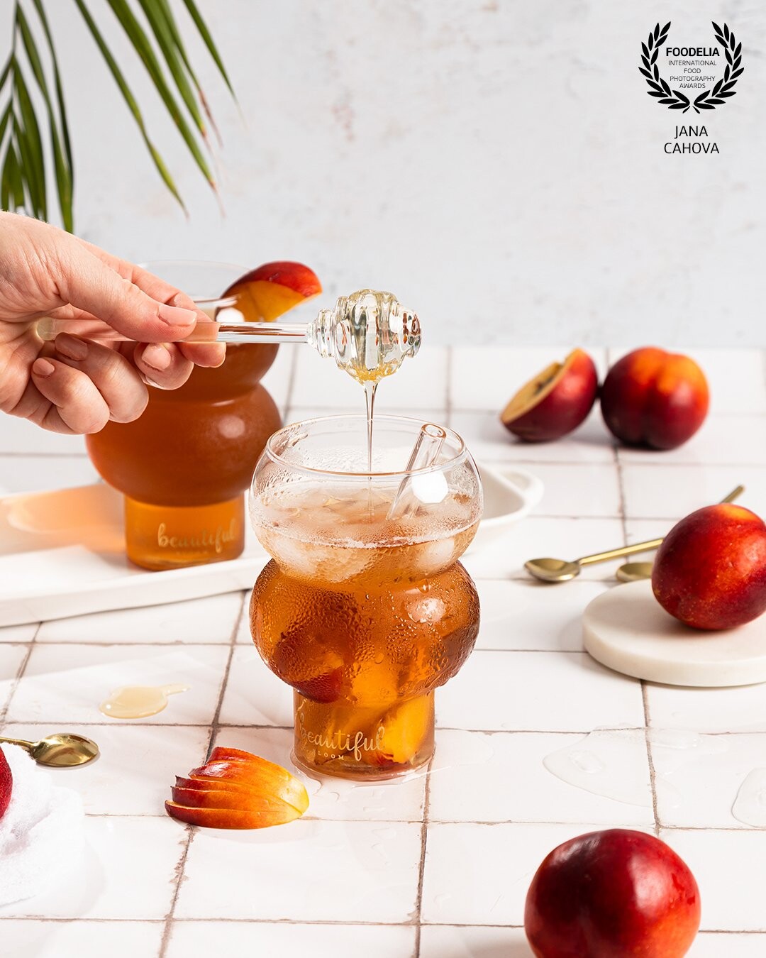 In this picture I wanted to emphasize simple color pallete. Brigthness, warm colors and a light setting gives the feeling of perfect summer. Peach iced tea for a super hot day... Ice cubes, palm leaf and golden details to complement the setting.