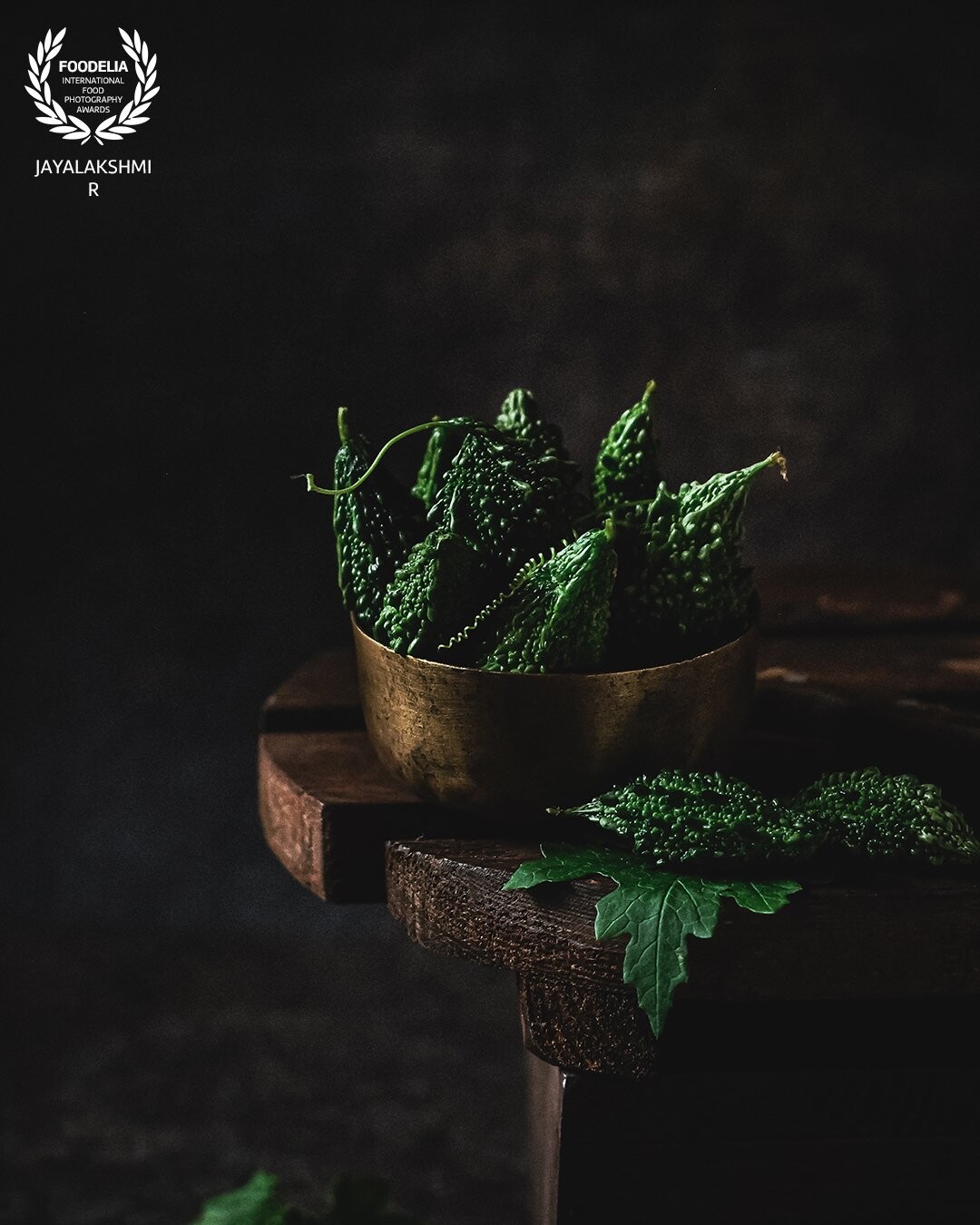 Fresh homegrown bitter gourd shot in a rustic moody frame. Used minimal props to highlight the green shades. The wooden stool adds the rustic tone to the frame.shot in natural light.