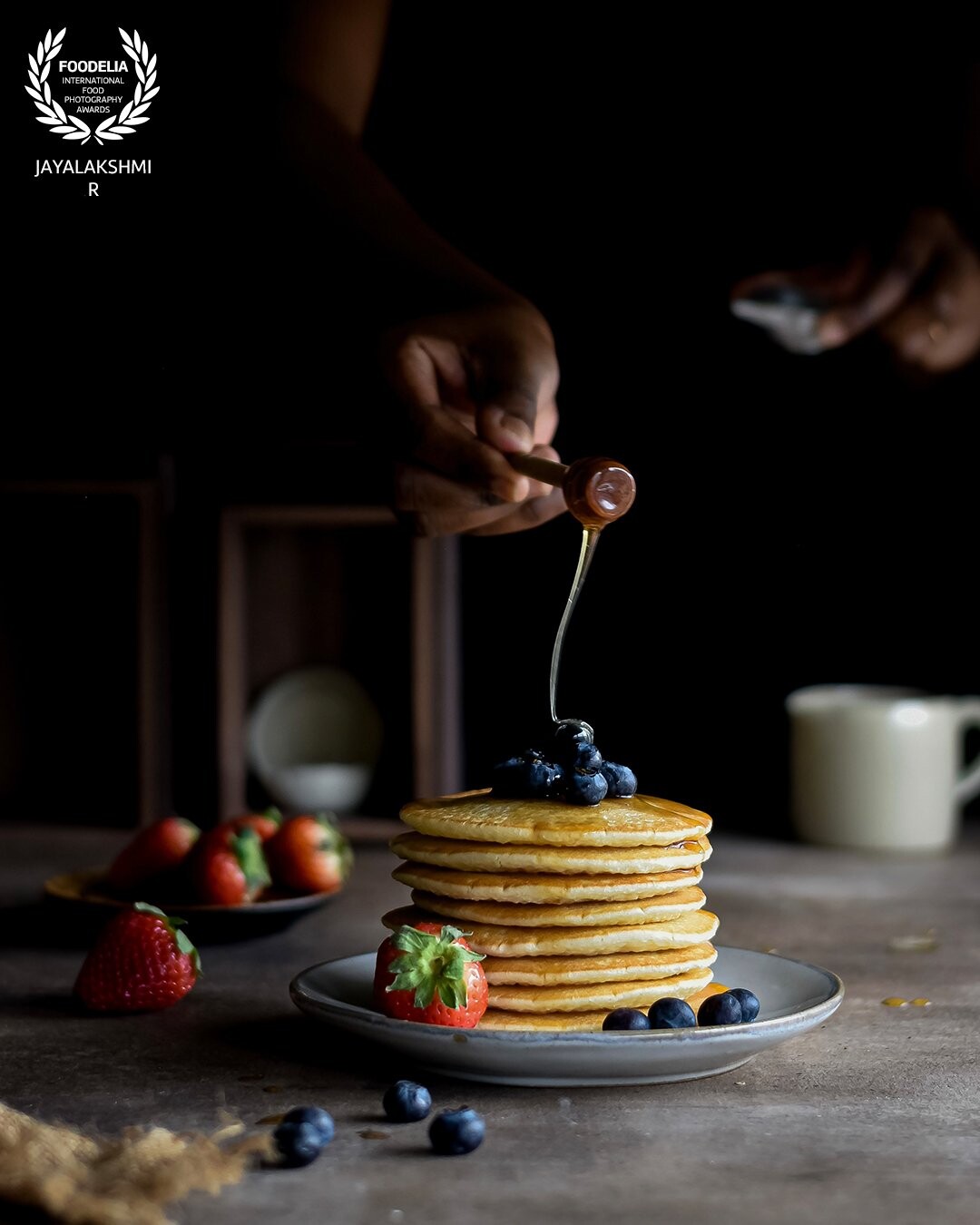 A typical breakfast scene. A stack of blueberry pancakes with a drizzle of maple syrup, loaded with fresh berries. Shot against a window in natural light.