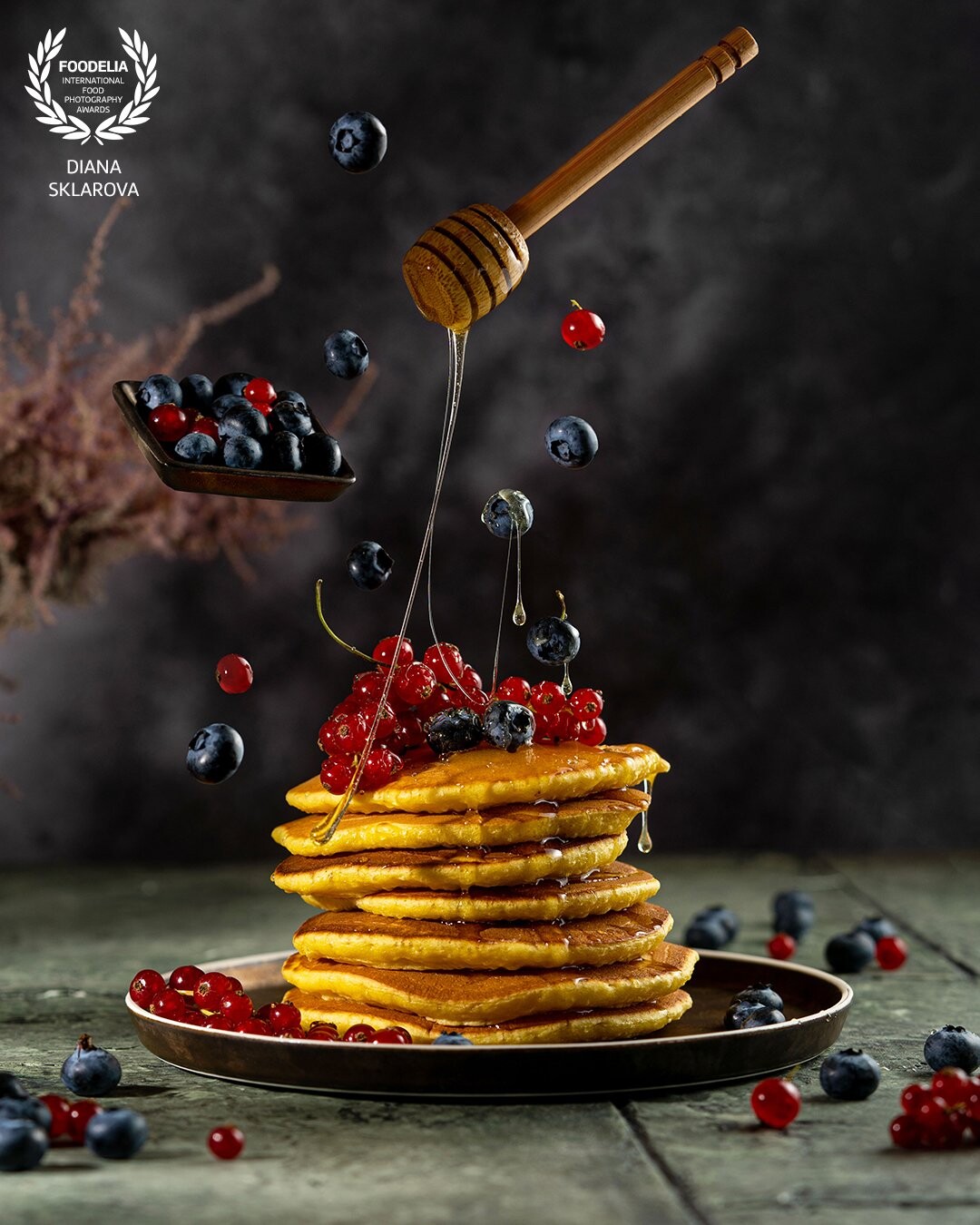 Homemade freshly baked pancakes with fresh berries and honey. Beautiful levitation art dessert photography on dark green textured table.