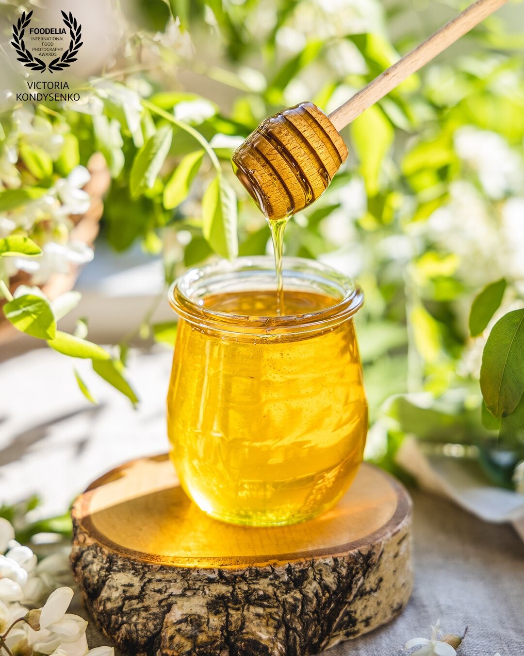 Sweet honey jar surrounded spring acacia blossoms. Honey flows from a spoon in a jar. Natural sunlight.<br />
Advertising shooting for a local farm
